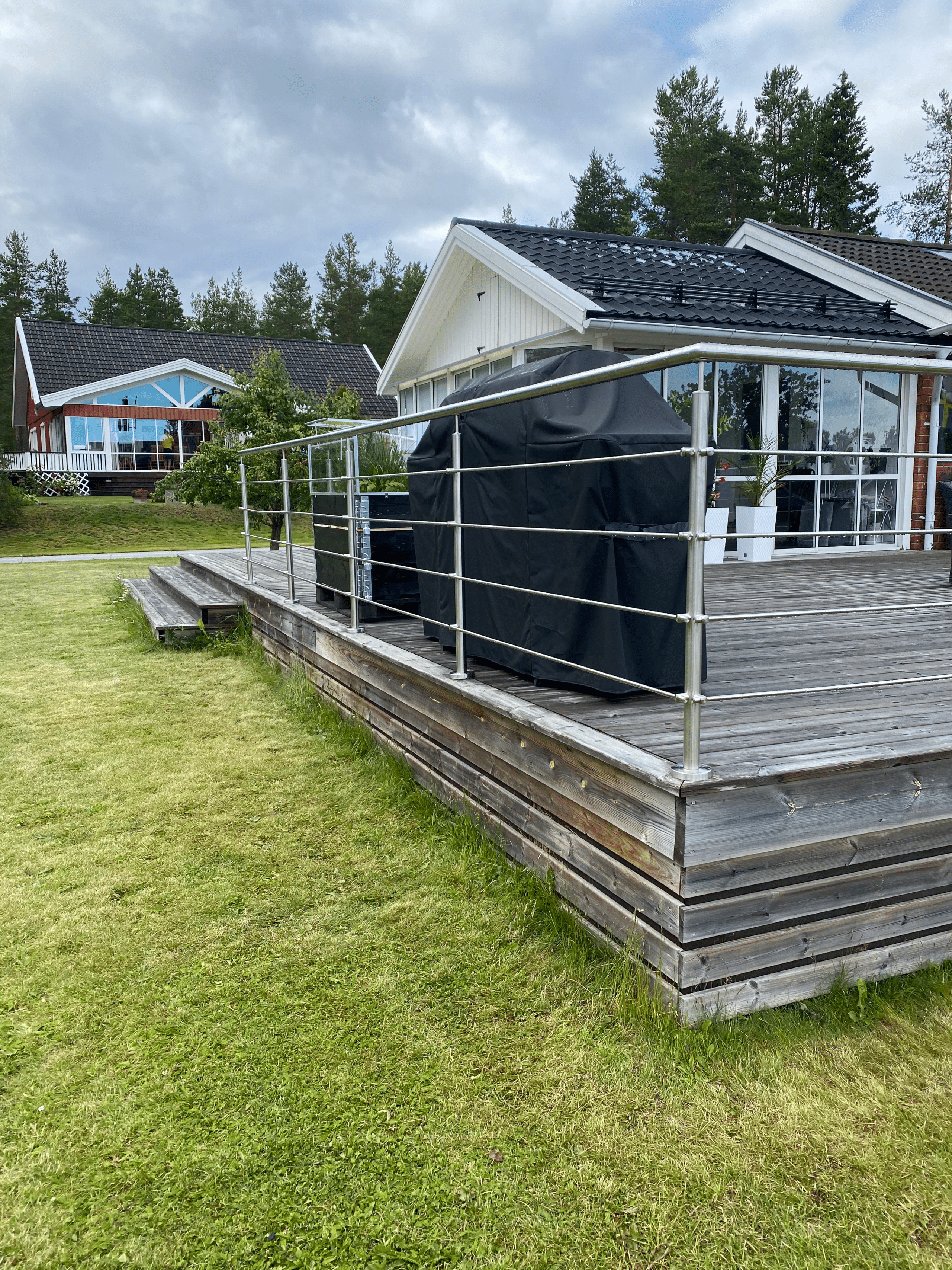 Terrasse en bois avec garde-corps à câbles horizontaux en inox, située devant une maison entourée de forêt.