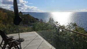 Garde-corps d’angle en verre avec main courante en bois et vue panoramique sur la forêt et la mer depuis une terrasse.