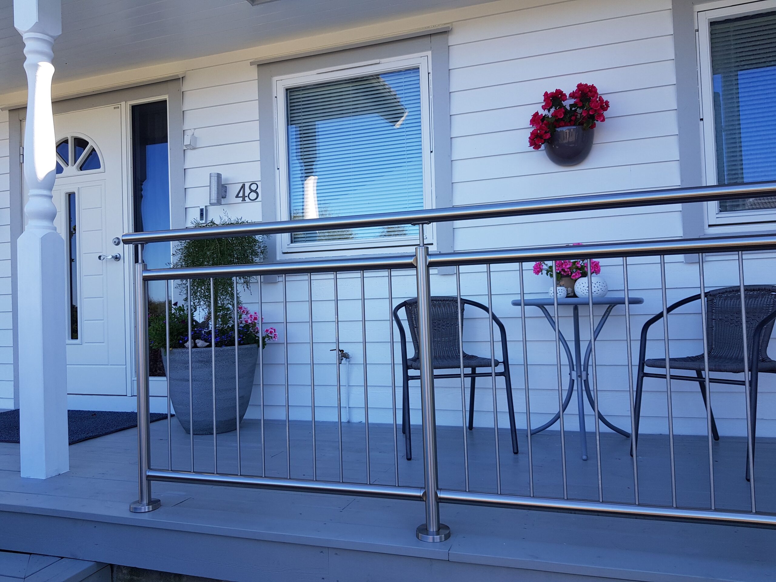 Garde-corps vertical en acier inoxydable monté près d’une véranda avec deux chaises, une table et des pots de fleurs.
