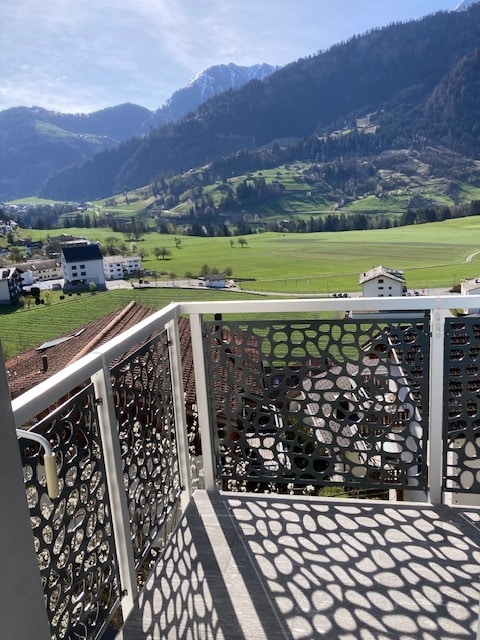Balustrade de balcon en métal découpé au laser à motif naturel, avec vue sur champs, montagnes et village alpin.