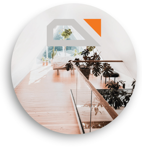 Garde-corps en verre avec main courante en bois clair dans une pièce lumineuse avec sol en bois et grandes plantes vertes.