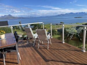 Terrasse avec garde-corps blanc en aluminium et verre clair, en bord de mer avec vue sur montagnes et horizon marin.