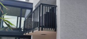 Garde-corps noir en acier avec barreaux verticaux sur un petit balcon, fixé à une façade blanche moderne.