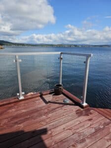 Garde-corps en verre clair avec poteaux en aluminium blancs sur terrasse rouge – vue sur mer et pont.