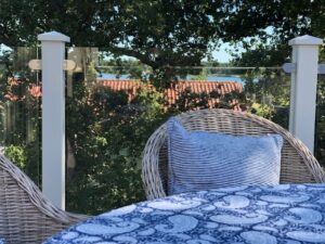 Garde-corps en aluminium blanc avec verre transparent sur terrasse, vue sur arbres et toits rouges en arrière-plan.