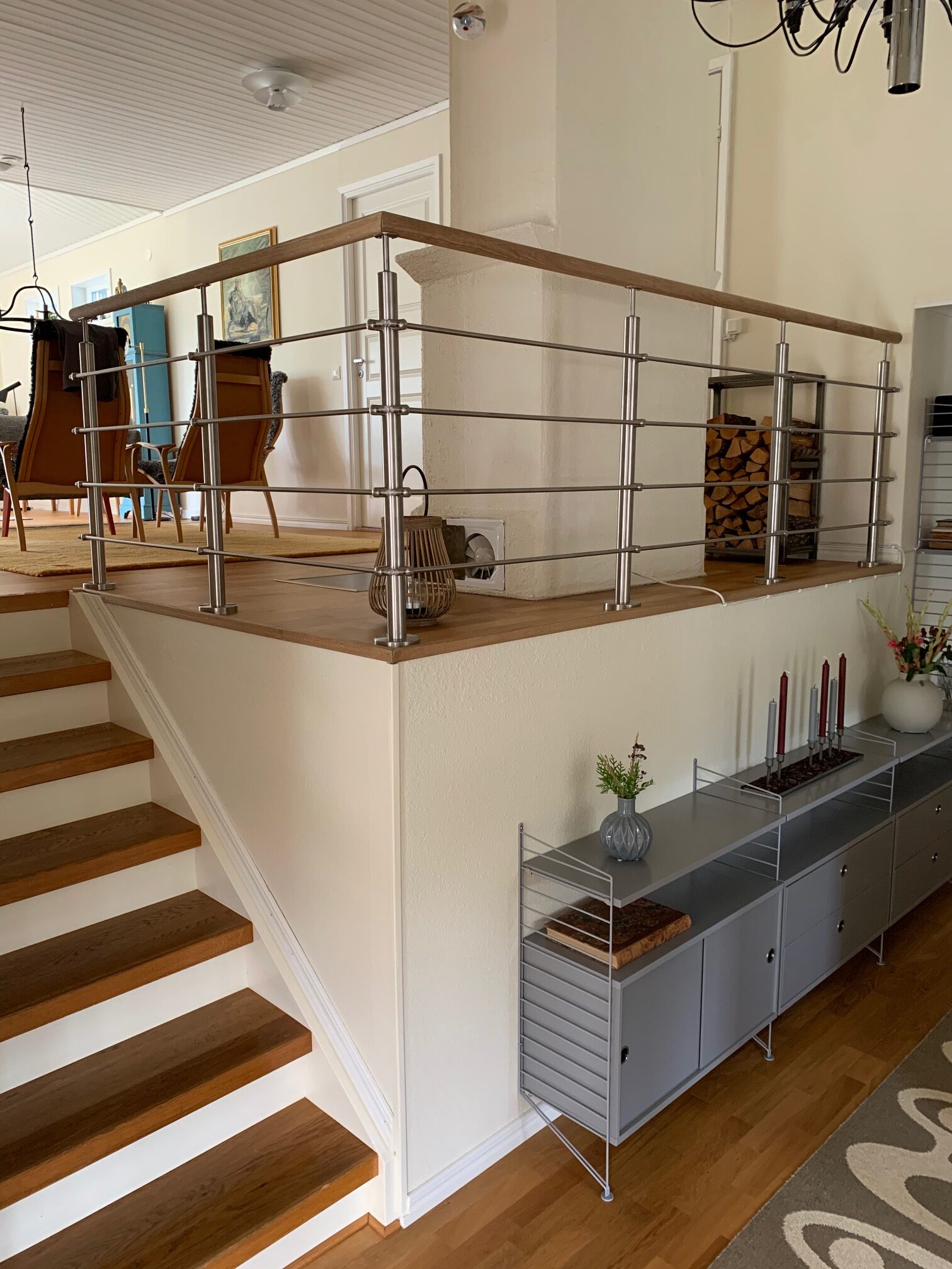 Garde-corps en inox avec main courante bois près d’une trémie d’escalier dans salon avec escalier bois et mur blanc.