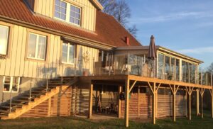 Garde-corps en inox avec verre clair monté le long d’un escalier et terrasse boisée avec véranda et soleil.