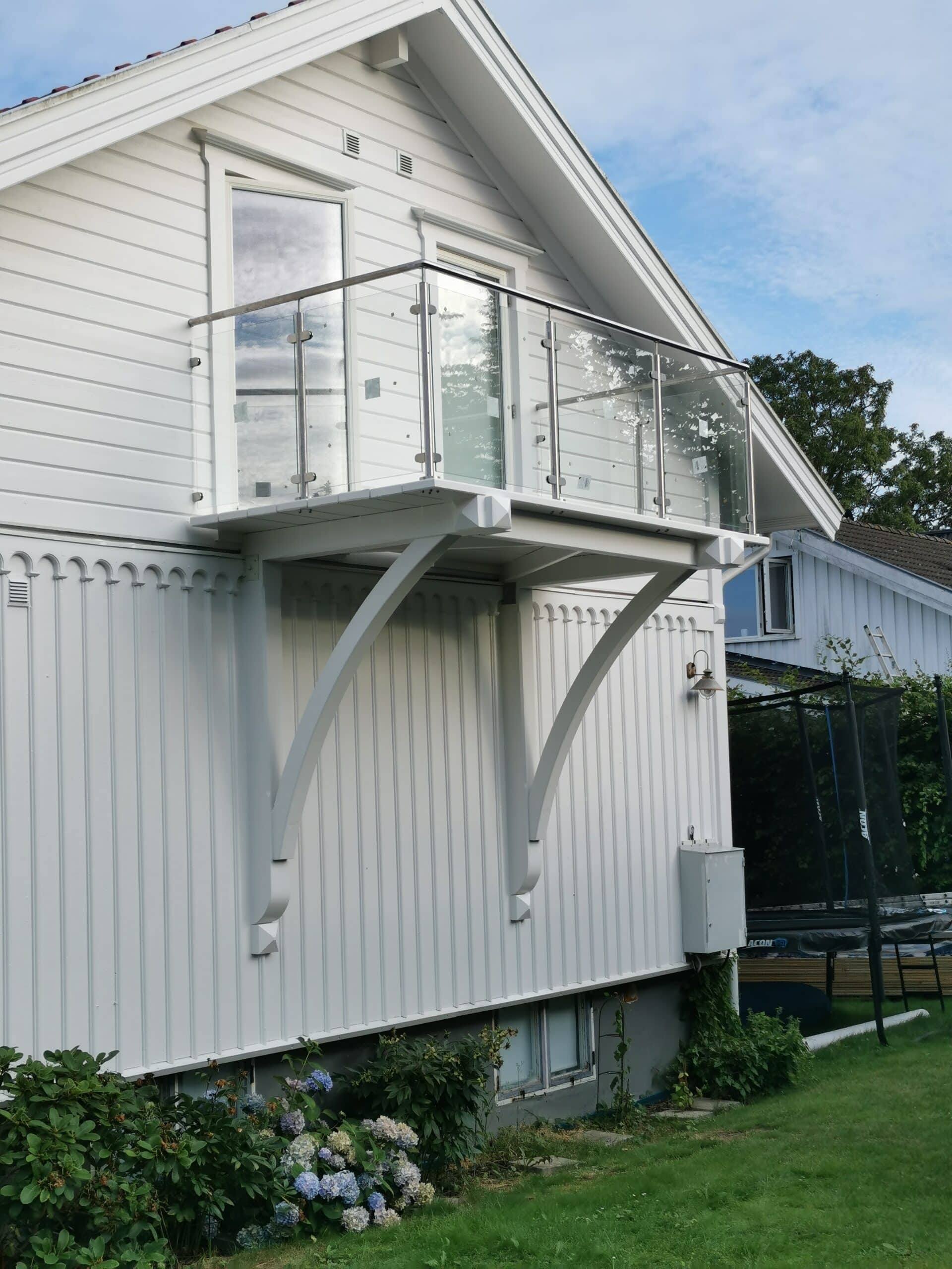 Rambarde contemporaine en inox et verre installée sur petit balcon d’une maison en bois blanc, assurant sécurité et vue dégagée